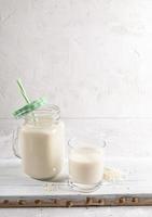 potabile bicchiere e bicchiere muratore boccale con salutare riso latte su di legno tavola su bianca sfondo. foto