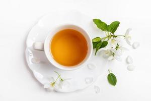 tazza di verde tè su immaginato piattino con bianca Mela albero fiori su bianca sfondo. superiore Visualizza. foto