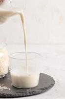 salutare riso latte scrosciante a partire dal bicchiere caraffa in potabile bicchiere su leggero sfondo. foto