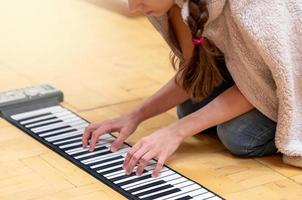 giovane ragazza giocando su pieghevole pianoforte tastiera su camera pavimento a casa. interessante attività su auto-isolamento. morbido messa a fuoco. foto