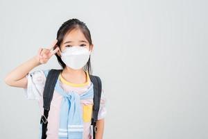 asiatico poco bambino ragazza trasportare un' zaino indossare respiratore maschera per proteggere coronavirus scoppio e puntamento mano per vuoto sfondo, nuovo virus covid-19 foto