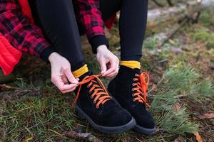 il ragazza è seduta su un' log nel il foresta e legatura luminosa lacci delle scarpe. viaggiare, il trekking e escursioni a piedi concetto. foto