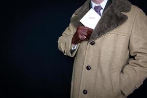 ritratto di uomo nel pelliccia cappotto e pelle guanti traino confidenziale Busta su di tasca su nero sfondo. film noir segreto agente spiare. furto e crimine. foto