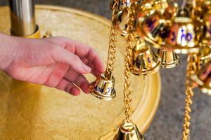 vicino su mano toccare piccolo d'oro campane nel tailandese tempio foto