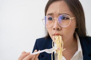 occupato e stanco donna d'affari mangiare spaghetti per pranzo a il scrivania ufficio e Lavorando per consegnare finanziario dichiarazioni per un' capo. oberati di lavoro e malsano per pronto pasti, bruciato concetto. foto