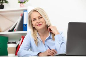 sua lavoro è sua vita. attività commerciale donna Lavorando nel ufficio con documenti. bellissimo mezzo anziano donna guardare a telecamera con Sorridi mentre ubicazione nel il ufficio. foto