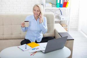 ascoltando per clienti requisiti. bellissimo mezzo anziano donna con bicchieri parlando su inteligente Telefono e sorridente a sua Lavorando posto ubicazione nel il ufficio. foto