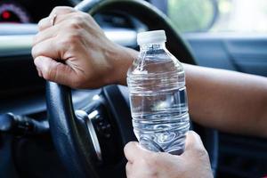 asiatico donna autista hold freddo acqua per bevanda nel macchina, pericoloso e rischio un incidente. foto