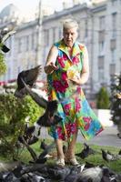 un anziano donna feed piccioni su un' città strada. foto