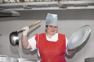 un' donna cucinare nel un industriale cucina con un' grande mestolo tra metallo padelle. capocuoco a il ospedale foto