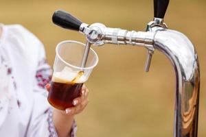 vicino su di il mano scrosciante un' boccale di schiumoso bozza birra a partire dal un' inossidabile acciaio birra rubinetto foto