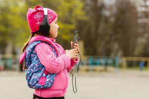 poco ragazza scolaretta. estate nel natura. nel mani Tenere un' smartphone ascoltando per musica su cuffia. prendere un' immagine su Telefono, parlando su il video chiamata. emozione sorrisi felicemente. foto