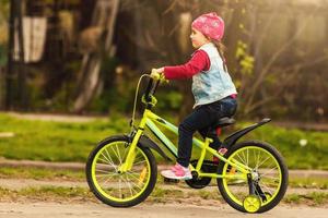 bellissimo sorridente poco ragazza equitazione bicicletta nel un' parco foto