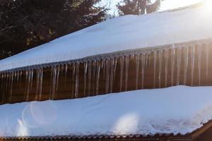 ghiaccioli sospeso a partire dal il bordo di di legno tetto foto