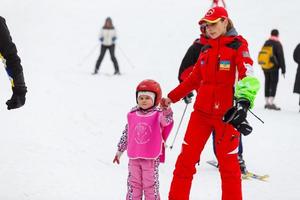 kiev, Ucraina - febbraio 02, 2018 poco ragazza nel rosso apprendimento per sciare con il Aiuto di un adulto foto