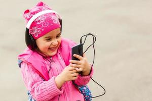 poco bellissimo ragazza gode il Telefono. lei cuffia. bambini e tecnologia foto