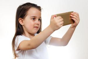 infanzia e tecnologia. bella poco ragazza assunzione autoscatto di sua smartphone. isolato su bianca. foto