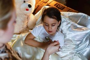 bambina malata a letto prendendo medicine con il cucchiaio foto