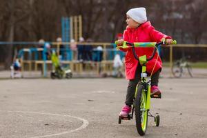 poco ragazza nel rosso equitazione un' bicicletta a un' sportivo terra foto