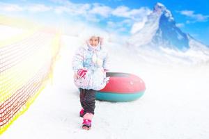 poco ragazza con tubo di neve pronto per slittino giù un' collina foto