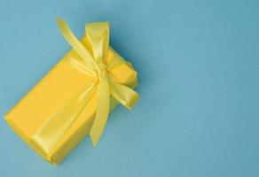 rettangolare scatola con un' regalo avvolto nel giallo carta e legato con un' seta giallo nastro foto