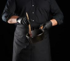 maschio cucinare nel nero uniforme e latice guanti detiene un vuoto il giro Vintage ▾ nero getto ferro padella foto