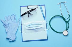 monouso medico maschera, plastica occhiali e stetoscopio su blu sfondo foto