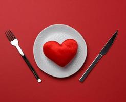 rosso cuore bugie nel un' bianca ceramica piatto su un' rosso sfondo foto