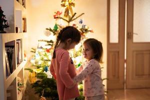 Due sorelle insieme vicino Natale albero a sera casa. foto