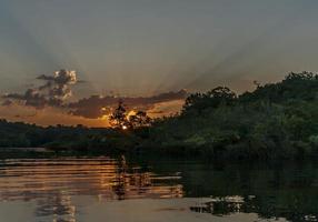 immagine di il tramonto al di sopra di il Amazonas prese a partire dal un' barca con degno di nota i raggi del sole e nube formazioni foto