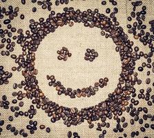 sorridente viso formato di caffè cereali su un' grossolano stoffa circondato di caffè fagioli foto