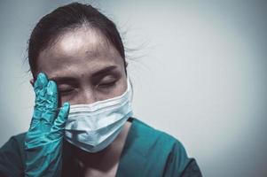 stanco depresso donna asiatica scrub infermiera indossa maschera facciale uniforme blu siede sul pavimento dell'ospedale, giovane donna medico stressato dal duro lavoro foto