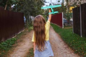 contento bambino ragazza con lungo biondo capelli giocando con giocattolo aereo all'aperto a tramonto foto