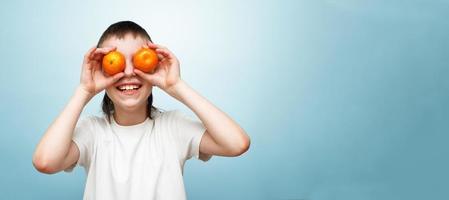 contento sorridente ragazzo con Due mandarini copertura il suo occhi su blu sfondo. foto