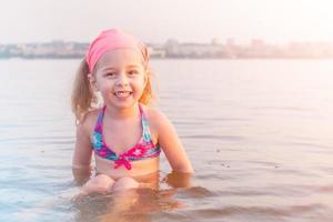 un' poco ragazza è bagnarsi nel il fiume nel il città. un' bambino nel un' costume da bagno nel il acqua nel il estate. foto