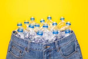 riciclare tecnologia di plastica bottiglia per rendere Abiti. superiore Visualizza vecchio acqua bottiglia e blu corto jeans su giallo foto