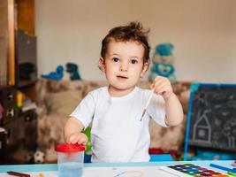 un' piccolo ragazzo si siede su un' sedia e disegna con colorato vernici foto