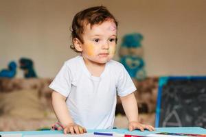 un' piccolo ragazzo disegna con colorato marcatori su un' pezzo di carta foto