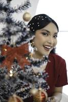 ritratto di bella giovane ragazza decorazione Natale albero, sorridente indossare rosso toga nel decorato Natale vivente camera in casa foto