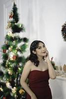 ritratto di un' bella giovane ragazza indossare un' rosso abito, sorridente a il telecamera, in piedi nel decorato Natale vivente camera in casa foto