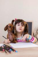 carino poco ragazza disegna con sua amico cane bassotto. bambini e animali. cane amichevole. alto qualità foto