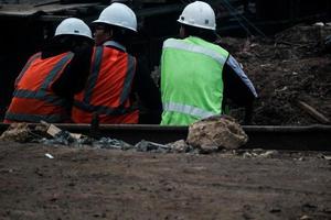 Giacarta, Indonesia nel luglio 2022. tre costruzione lavoratori siamo riposo per rilassarsi dopo opera di seduta su il bordo di il costruzione luogo foto