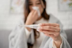 avvicinamento di mano Tenere corpo temperatura dai un'occhiata a casa. asiatico donna coperto con coperta lei si sente freddo. influenza concetto. foto