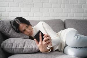 preoccupato giovane donna pianto dire bugie su divano Tenere e Guarda Telefono in attesa per chiamata Messaggio. lei è triste dopo un discussione con sua fidanzato. foto