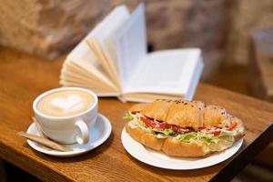 delizioso brioche con caffè e un' libro su il tavolo foto