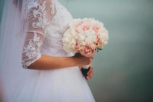 la sposa in un elegante abito da sposa tiene un bellissimo mazzo di fiori diversi e foglie verdi. tema del matrimonio foto