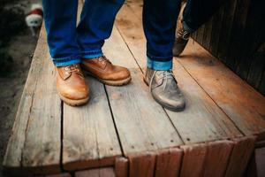 ritagliata foto giovane gambe nel elegante scarpe, sposato coppia, marito e moglie su un' di legno ponte vicino lago. posteriore Visualizza di coppia in piedi su molo.
