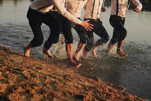 Uomini piedi nel il acqua. essi siamo avendo divertimento, giocando e spruzzi acqua in giro loro. uomini nel costumi correre su acqua. estate. gruppo di contento giovane uomo piedi spruzzo acqua foto