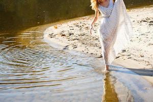 giovane donna nel bianca vestito a piedi solo su il spiaggia foto