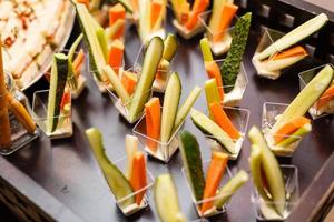 ristorazione per festa. vicino su di Antipasti con ciliegia pomodori, verde olive, oliva olio, formaggio e spezie nel corto bicchieri su legna Marrone tavolo. foto